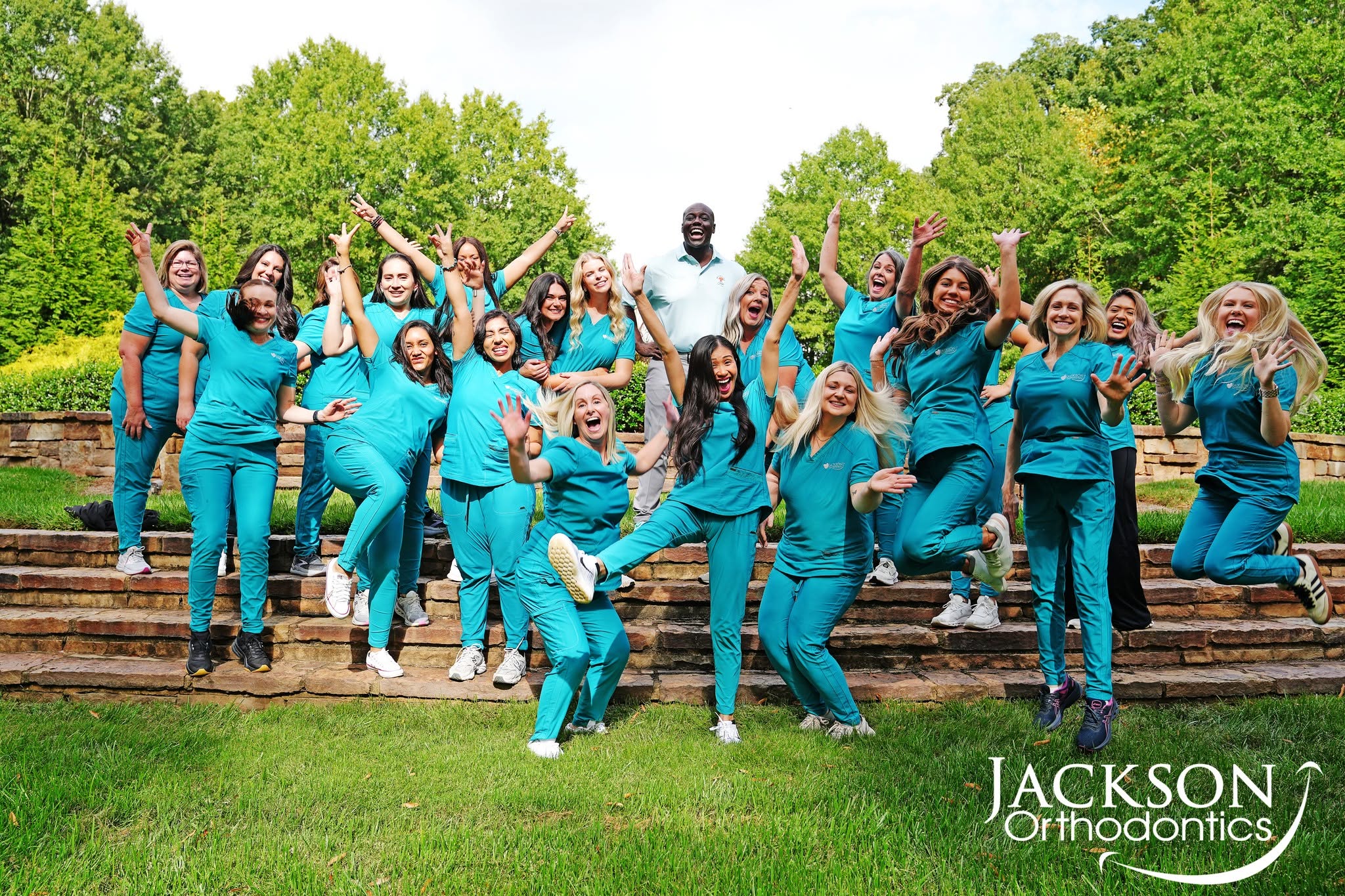 Dr. Jackson and the Jackson Orthodontics team jumping and celebrating outdoors on stone steps.
